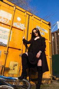 Wide angle portrait of model all in black against a yellow container