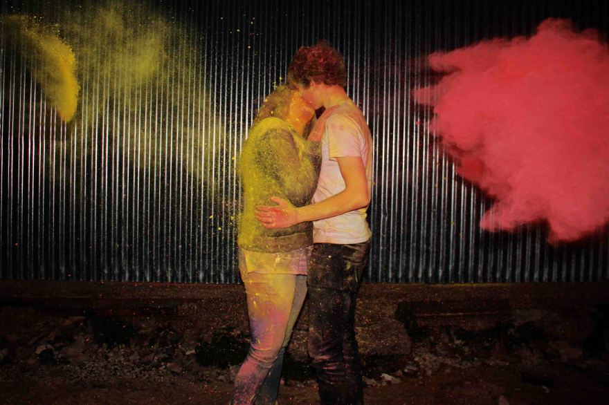 Couple kissing whilst red and yellow powder paint are thrown