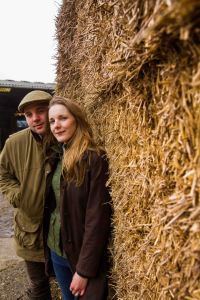 Country couple portrait with farmer and wife cuddling and hay to the right