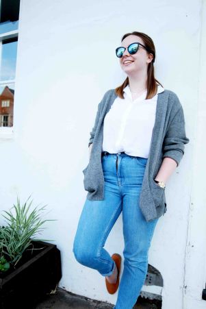 Blogger lifestlye portrait of model in highwaisted jeans, leaning against a wall wearing sunglasses