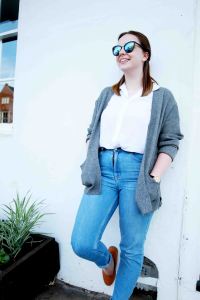 Blogger lifestlye portrait of model in highwaisted jeans, leaning against a wall wearing sunglasses