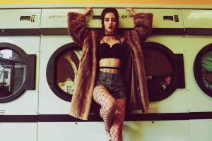 Model holds onto washing machines in a launderette wearing a fur coat