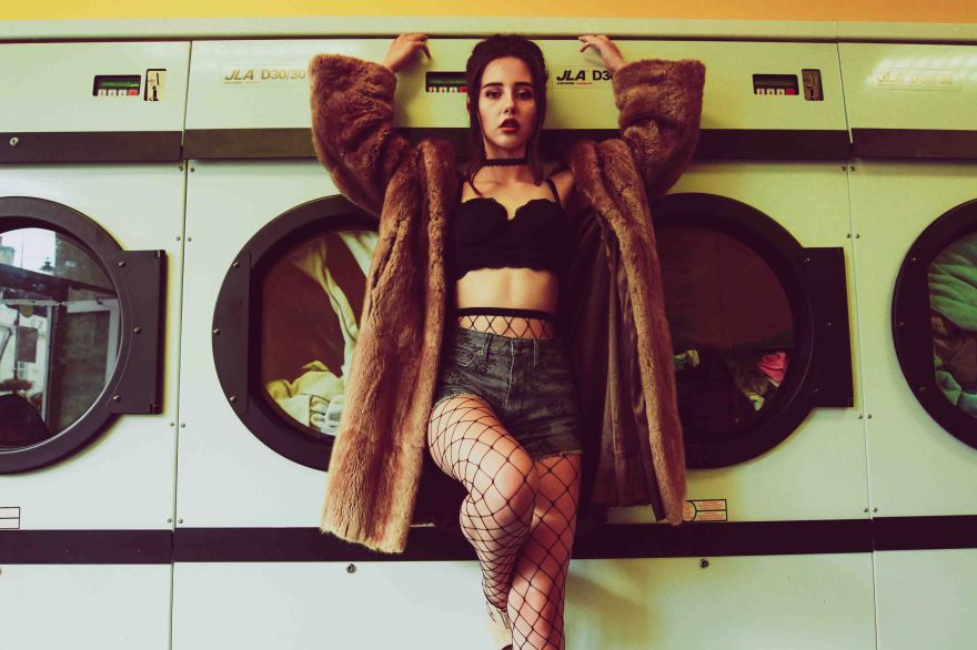 Model holds onto washing machines in a launderette wearing a fur coat