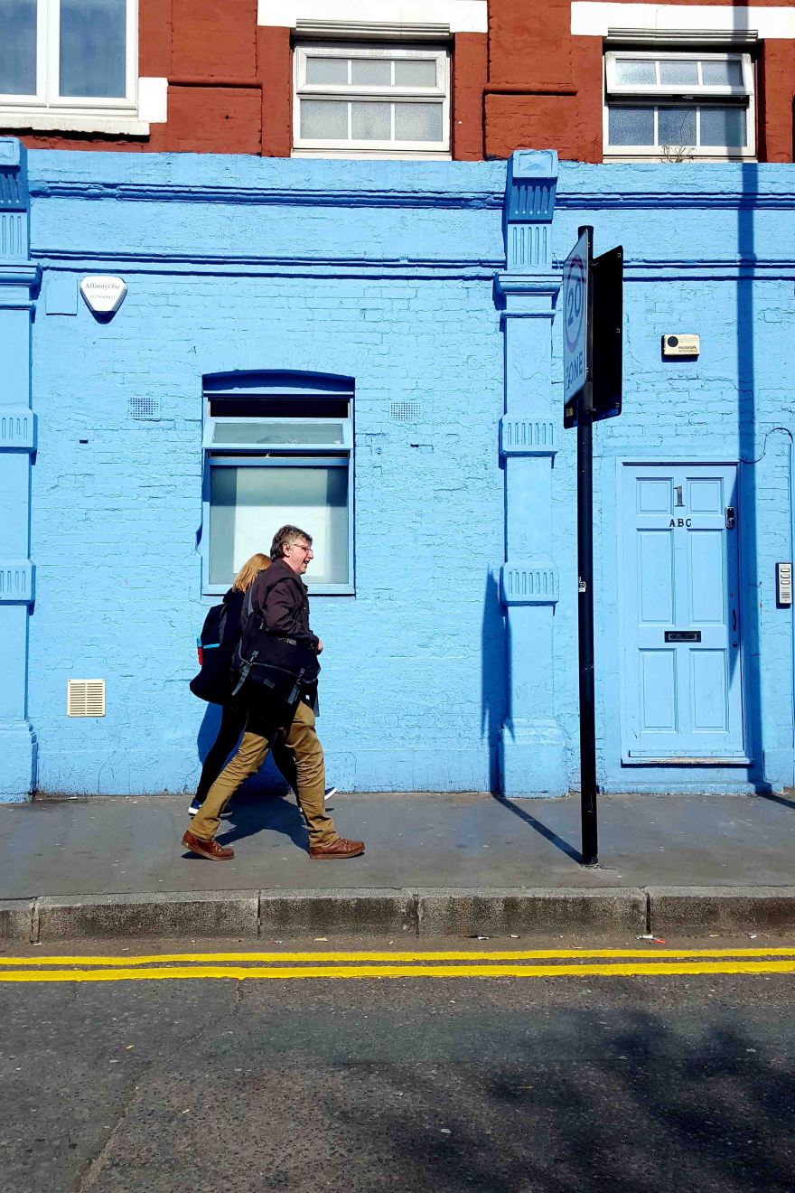 Street photography with people walking in front of a blue house