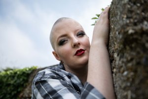Close up portrait of bald alternative model holding a wall