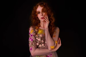 Red haired model holding her face in a floral dress