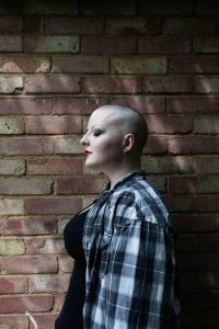 Side profile of bald model against a brick wall with flickers of light