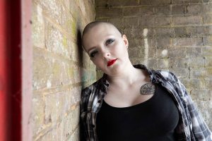 Bald alternative model leaning against a brick wall